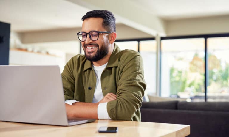 man with dark rimmed glasses smiling in front of laptop
