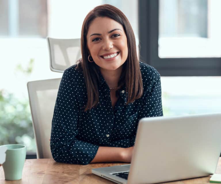 woman smiling looking straight ahead sitting in front of laptop at desk