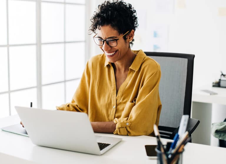 woman smiling looking down sitting in front of laptop at desk