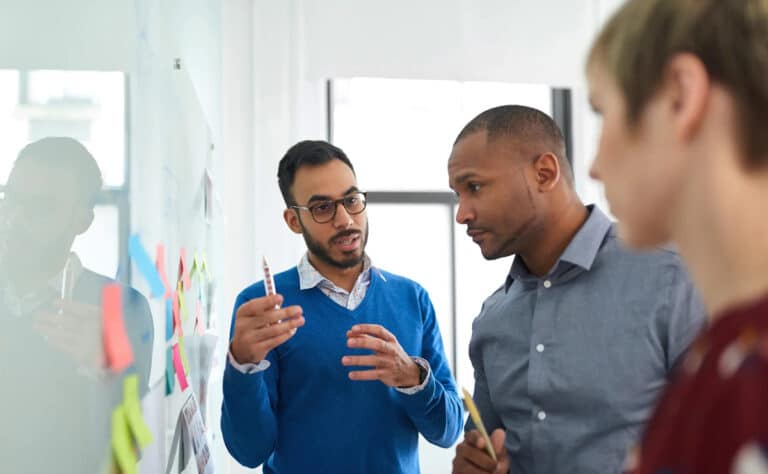 man at board with sticky notes explaining concept to two others