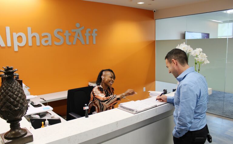 employee signing into the front desk at AlphaStaffHCM while the receptionist smiles