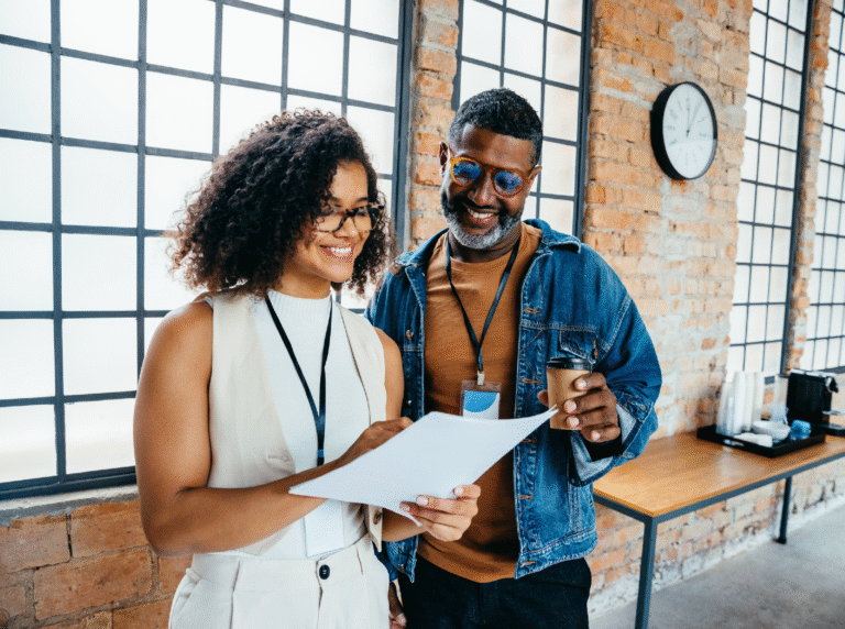 Man and woman standing next to each other in office looking at paper while man holds coffee.