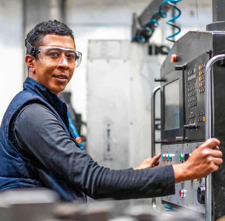 technician in front of machine interface with safety glasses and vest