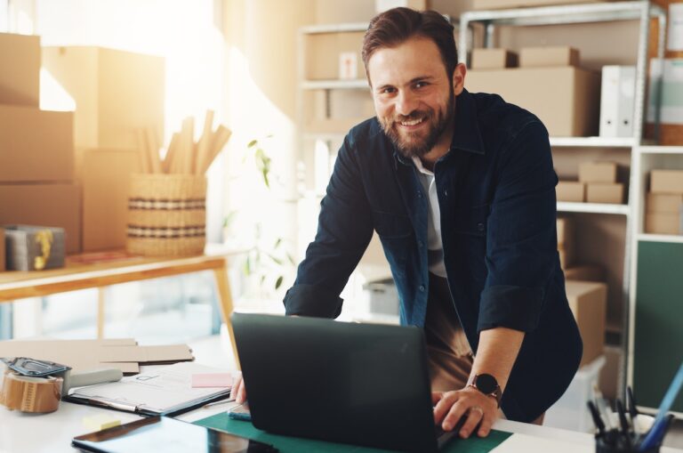 man smiling at the camera while standing over his laptop