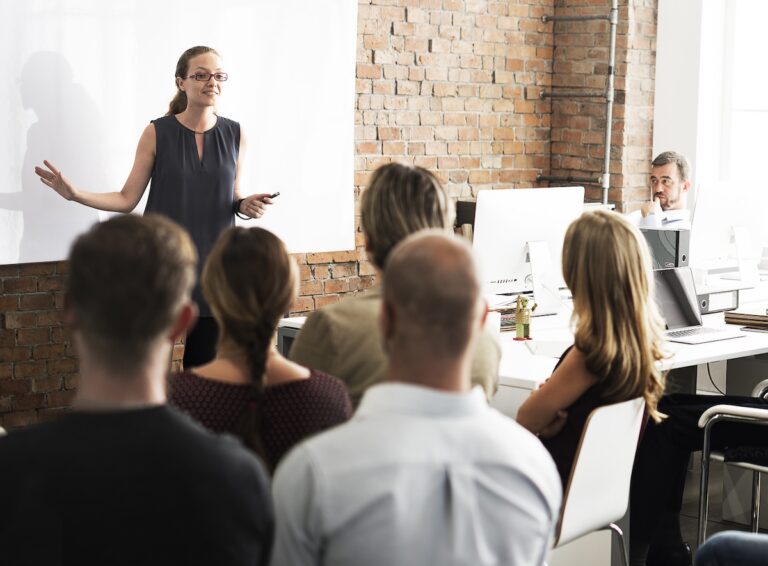 business team listening to team member speak at the front of the room