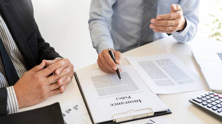 two people close up of hands at table with insurance policy papers and pen