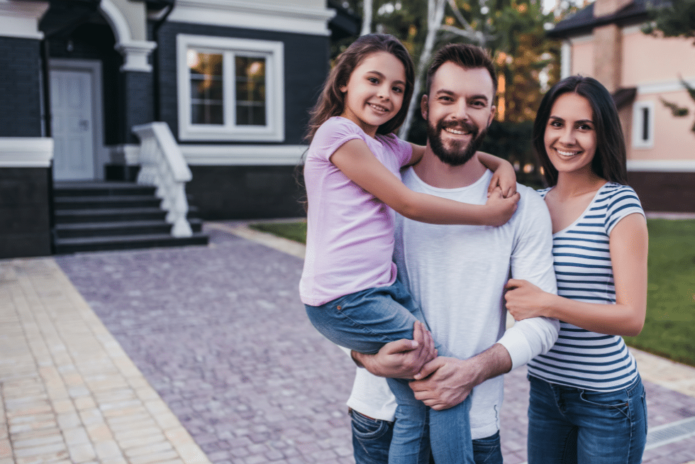 A husband and wife with a small child standing in front of a blue house.