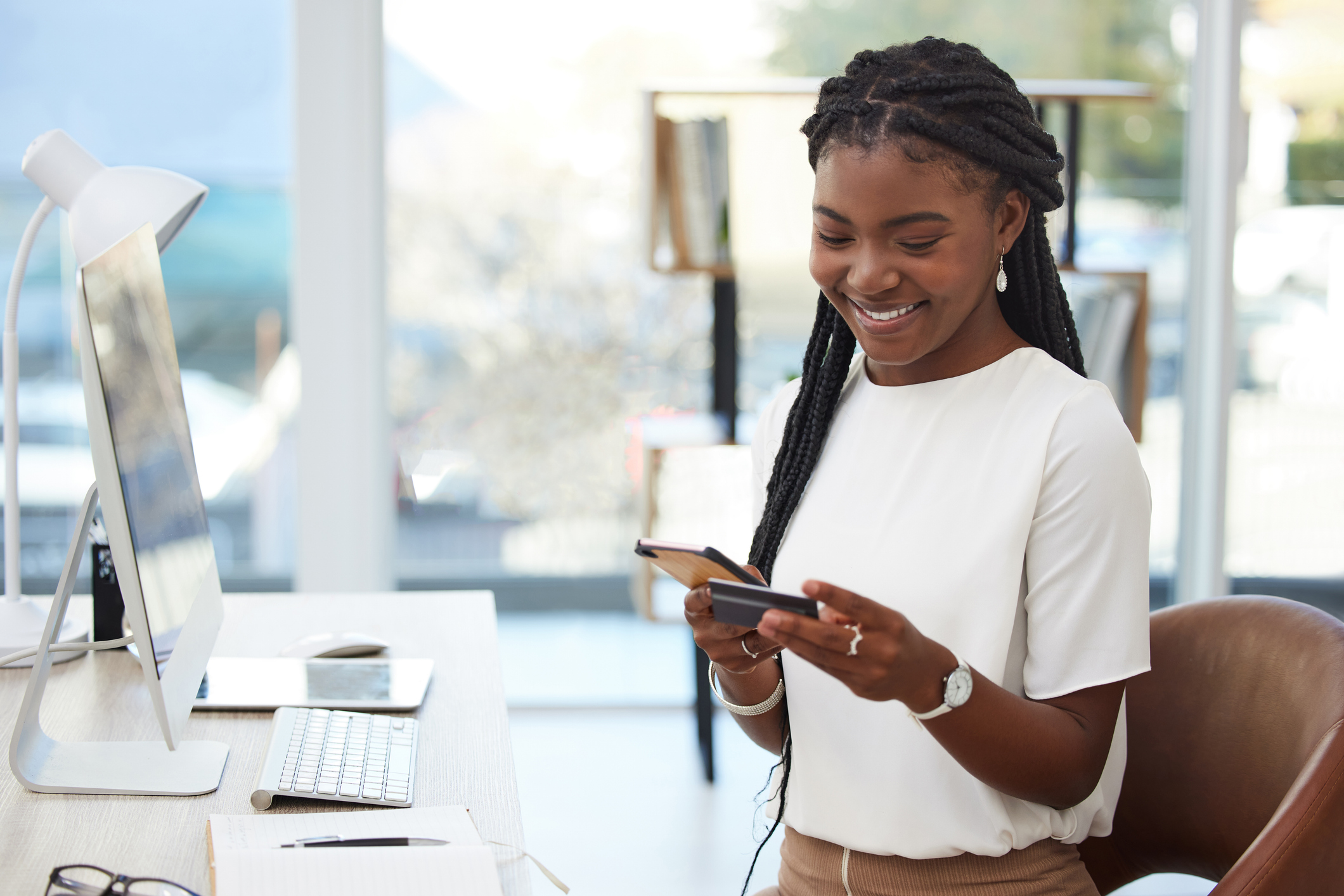 Shot of a young businesswoman using a credit card and phone at work