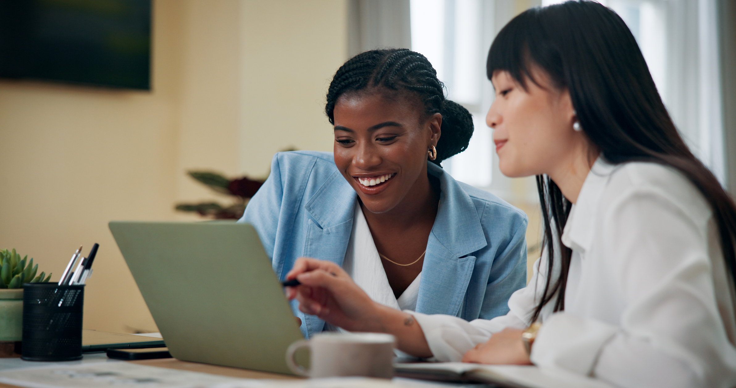 Two businesswomen working together on a laptop while one lady provides feedback to the other.
