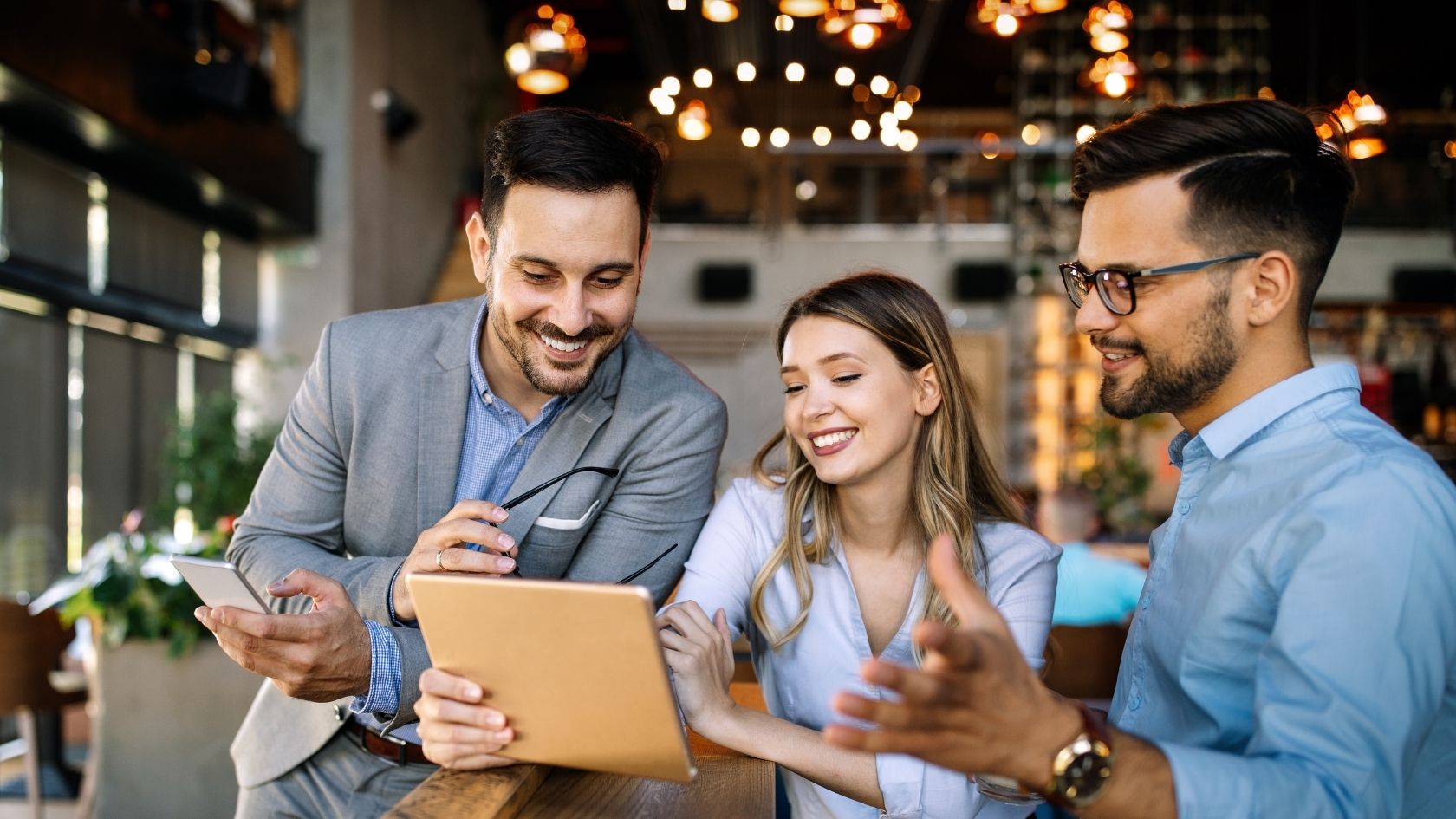 two male and one female coworker standing around an iPad smiling at what they are viewing