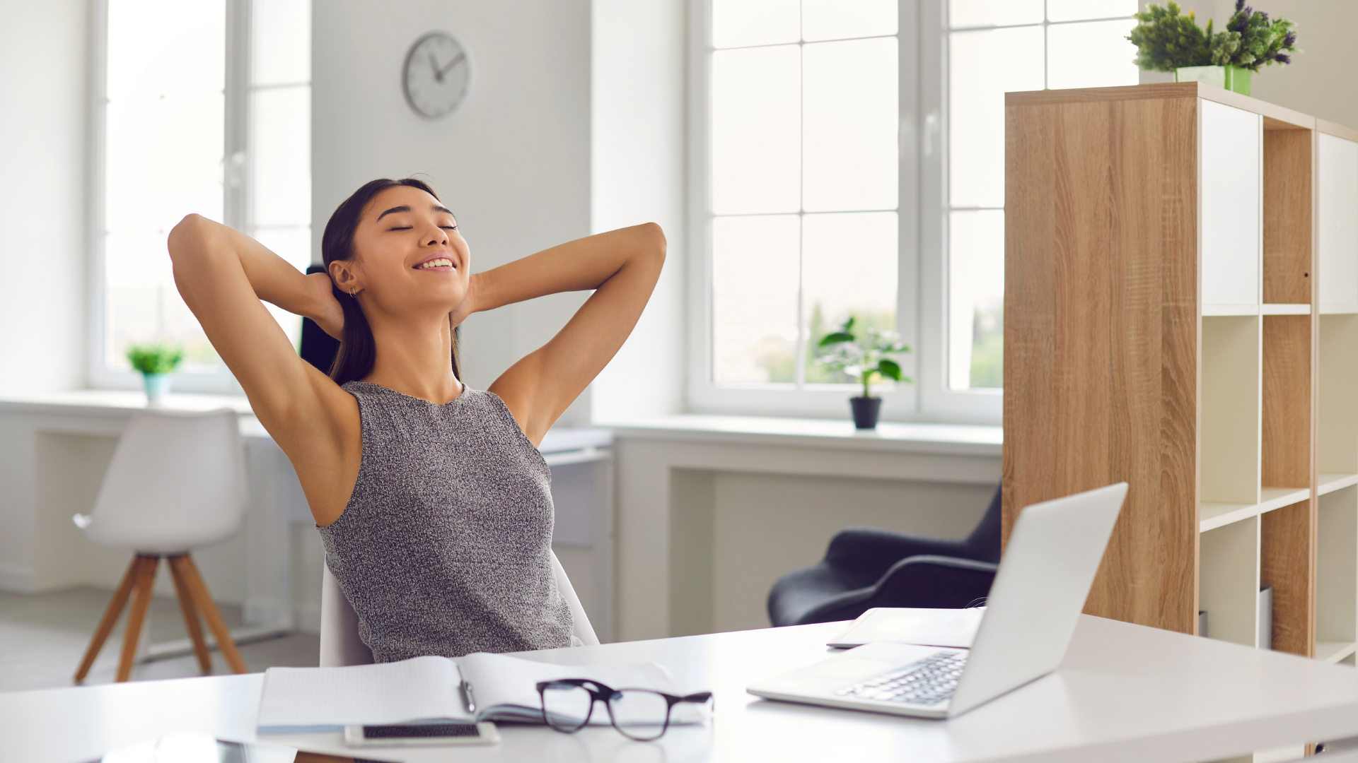 Employee leaning back in her desk chair, smiling while taking a break from working