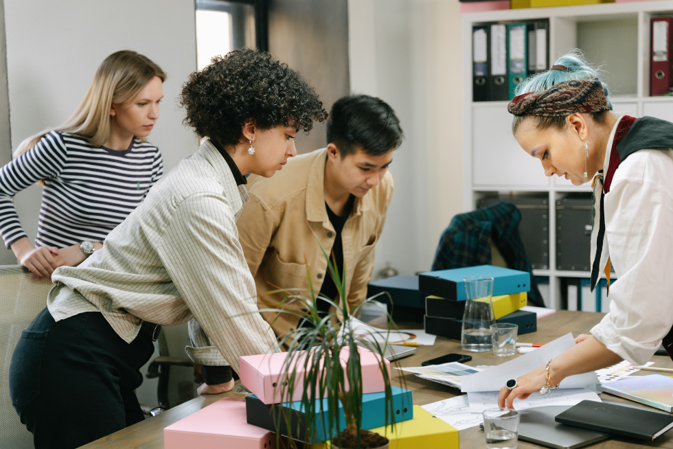 Four human resources professionals gathered around a desk reviewing employee documentation papers.