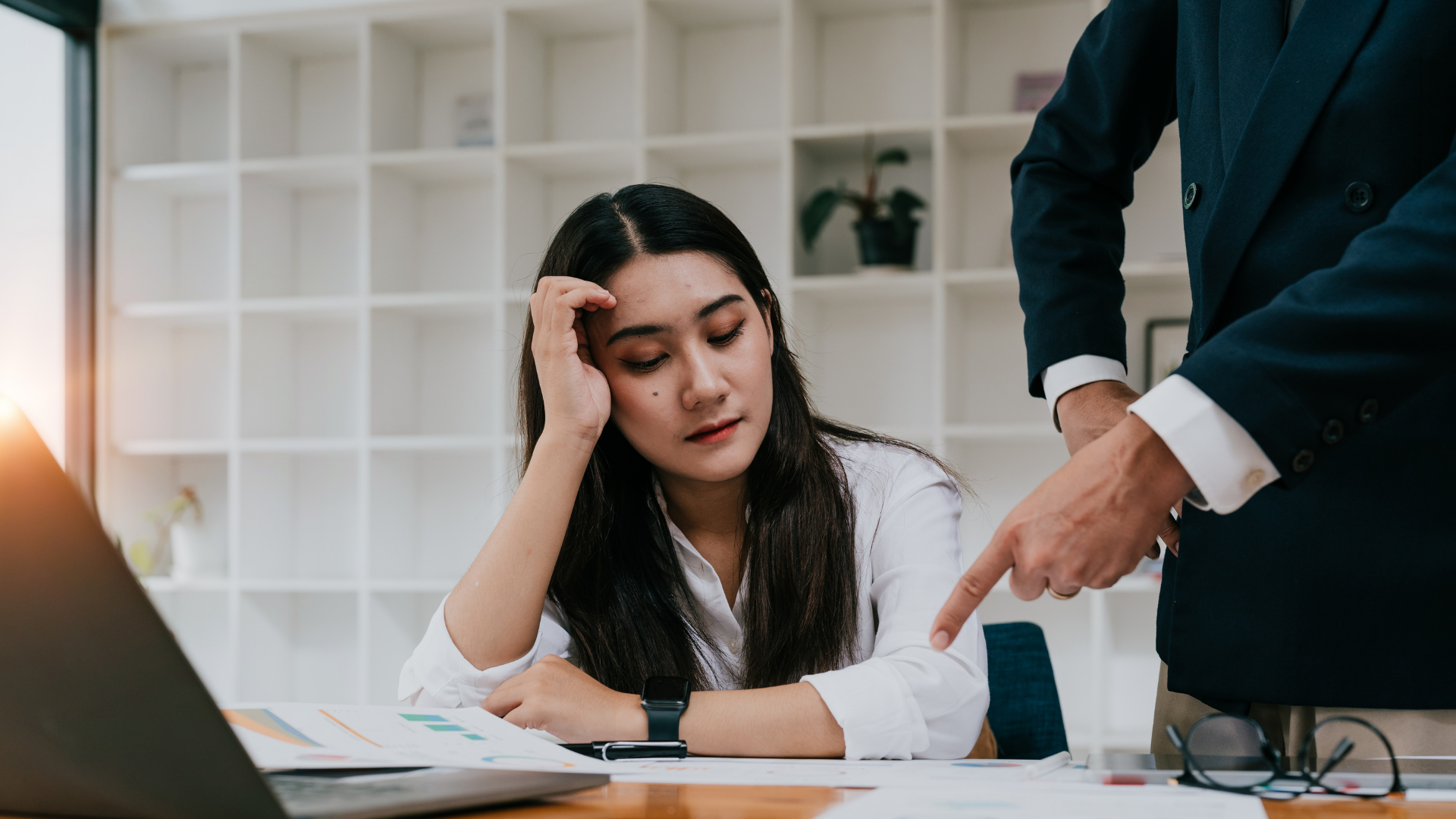 Employee frustrated at work while someone is pointing at her work in front of her