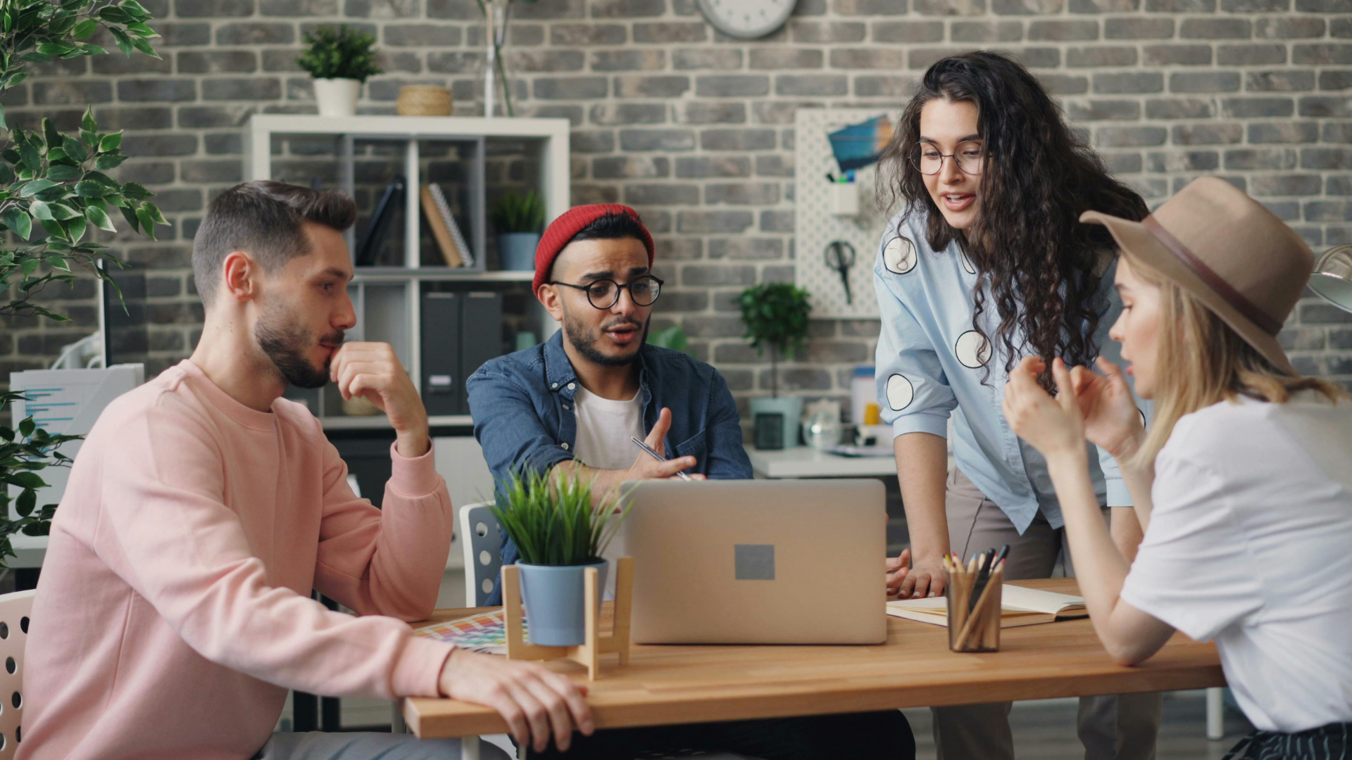 four coworkers sitting around a table while one male coworker shows something on his laptop to his female coworker