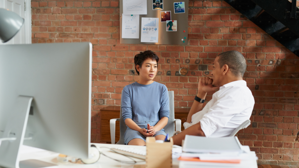 Two workers sitting together at a desk speaking