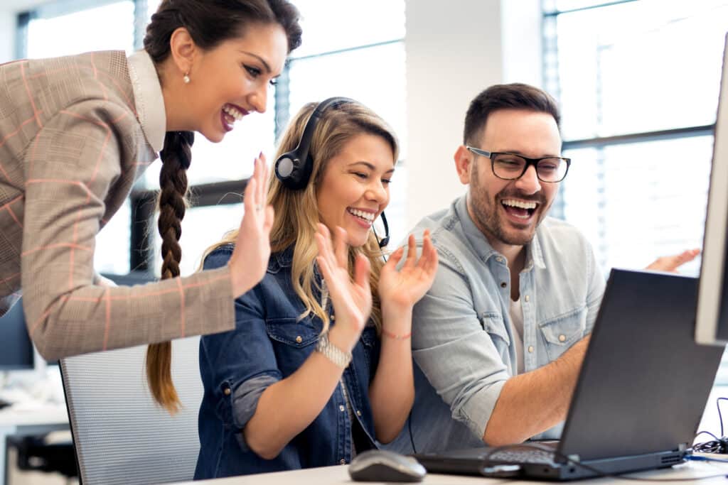 group of colleagues waving to someone in an online meeting on their laptop