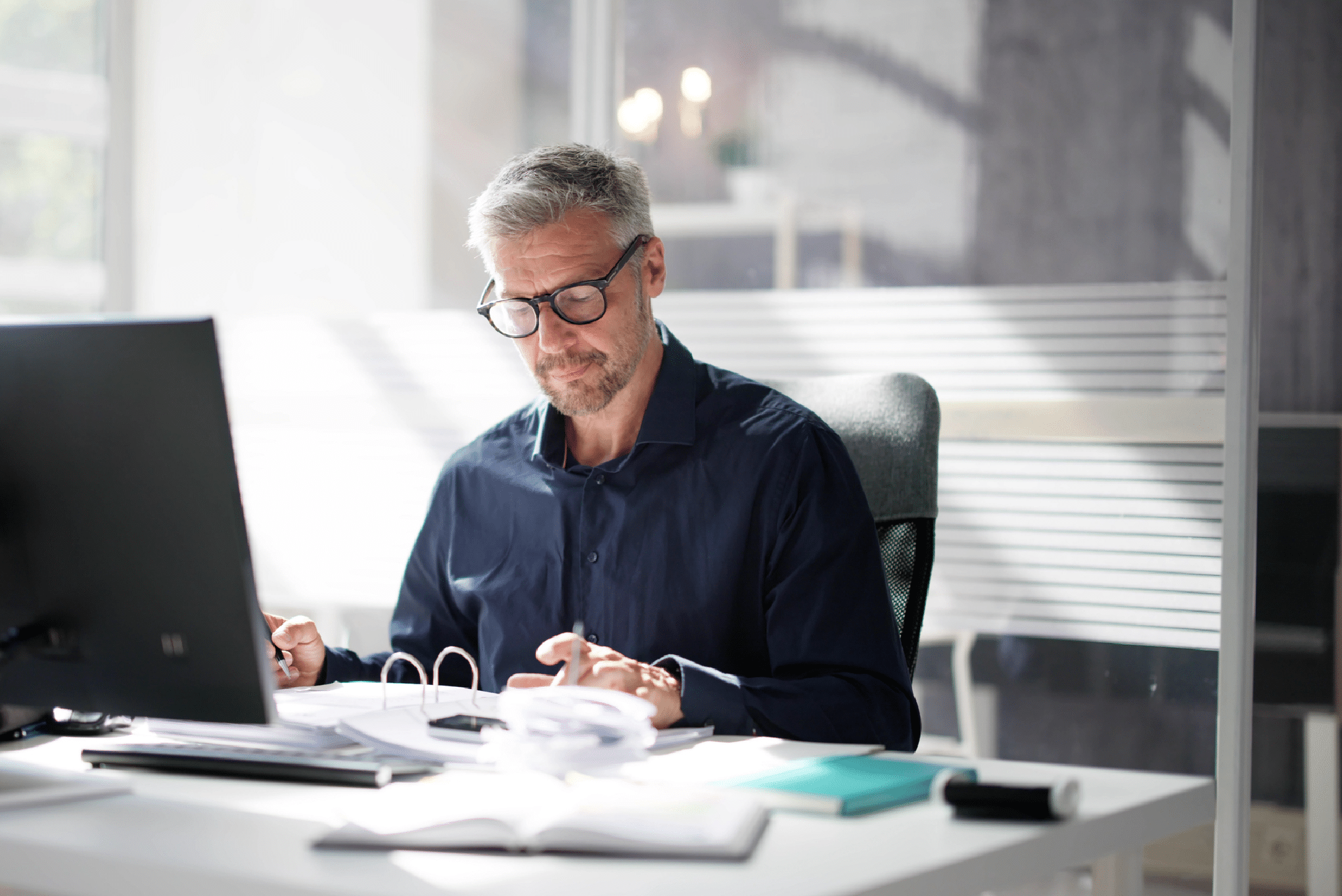 man sitting down in front of a computer reviewing items in a binder